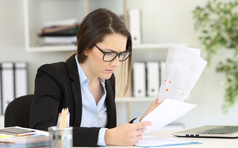 woman sitting at desk looking worried reading paperwork