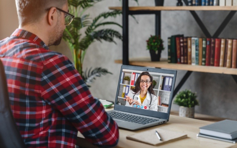 man sitting at desk talking to doctor on computer screen