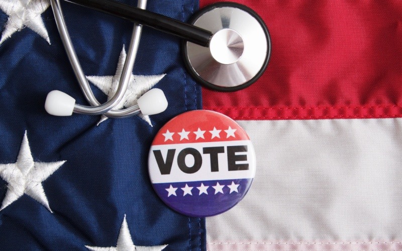 vote pin sitting on top of American flag with stethoscope