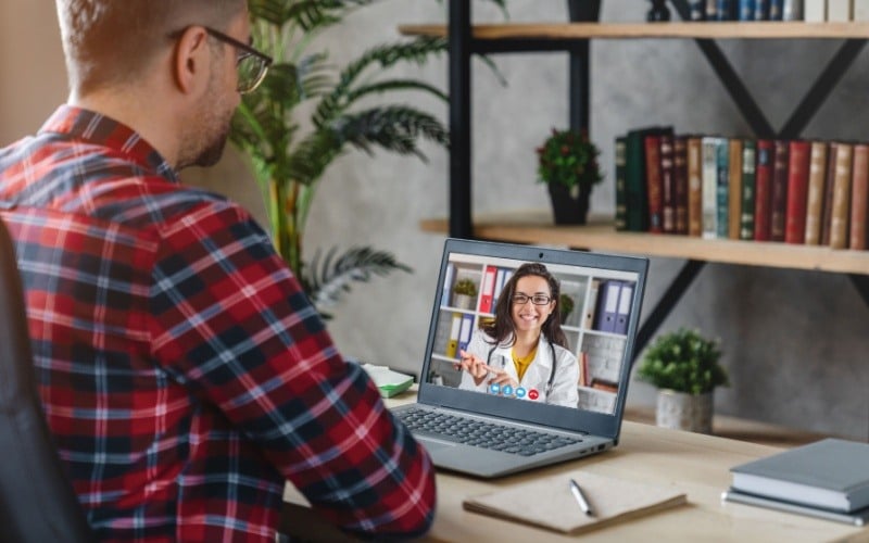 man sitting at desk talking to a doctor from a computer