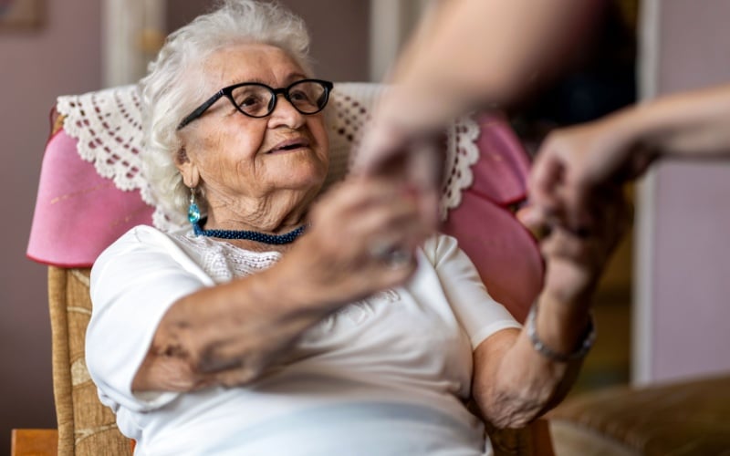older woman sitting in chair holding carer hands