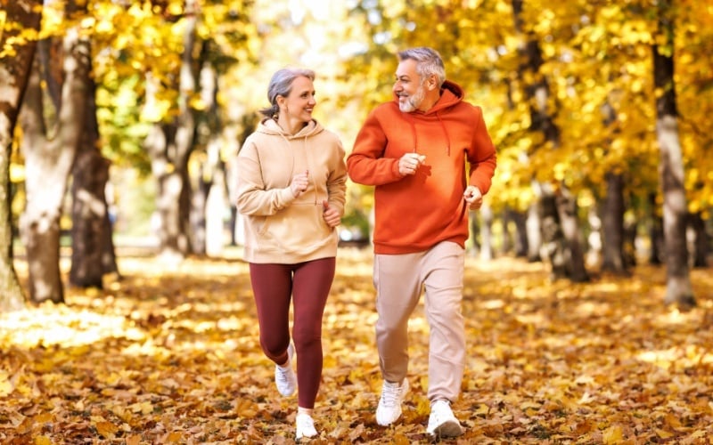older couple jogging in park in fall