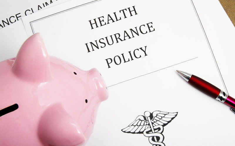 piggy bank sitting on top of health insurance policy