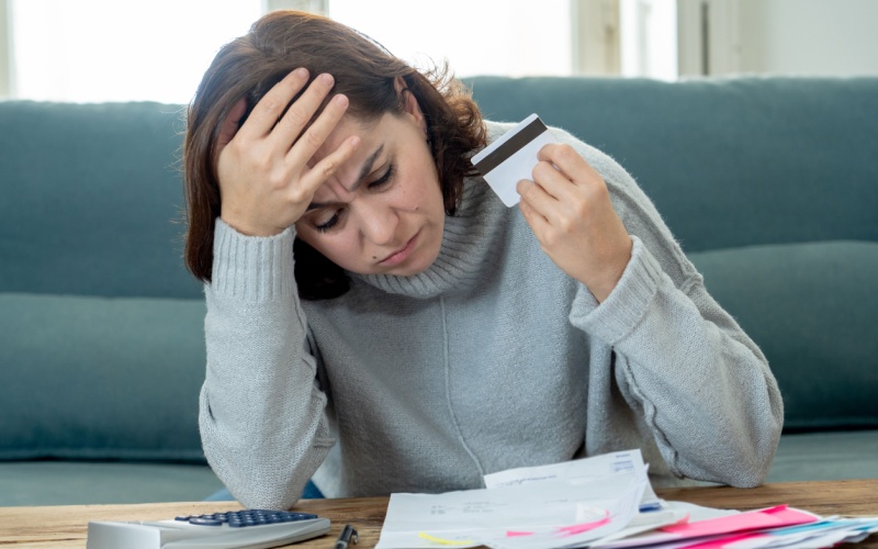 stressed woman sitting looking at paperwork holding credit card