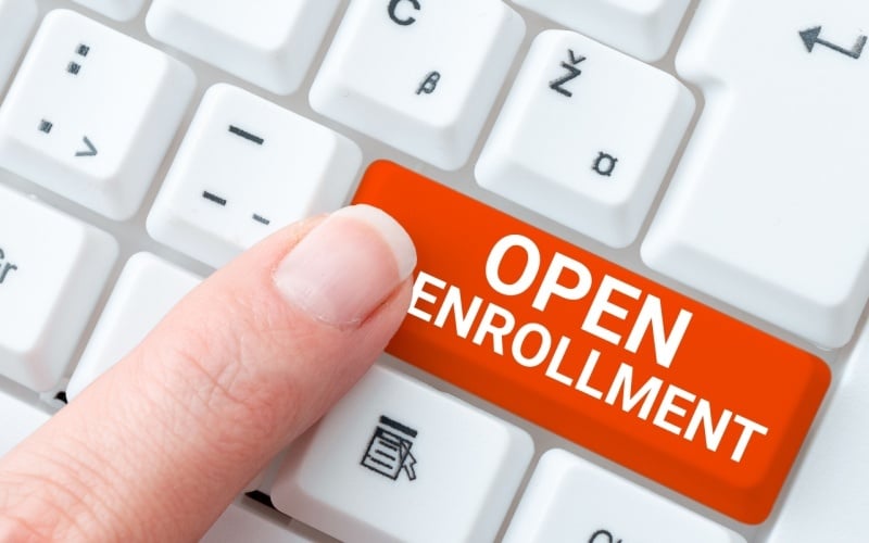 person pressing computer key that reads open enrollment