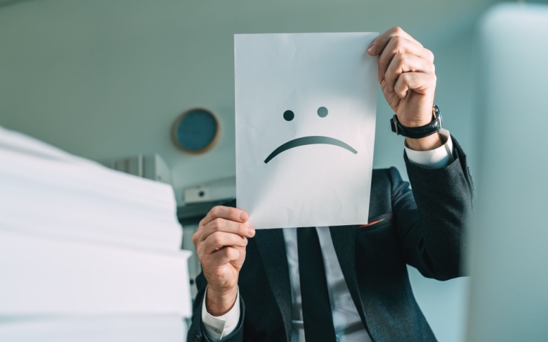 man holding up frowny face sign in front of his face
