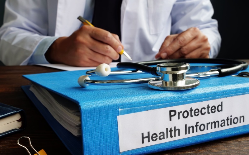 doctor sitting at desk with binder that reads protected health information