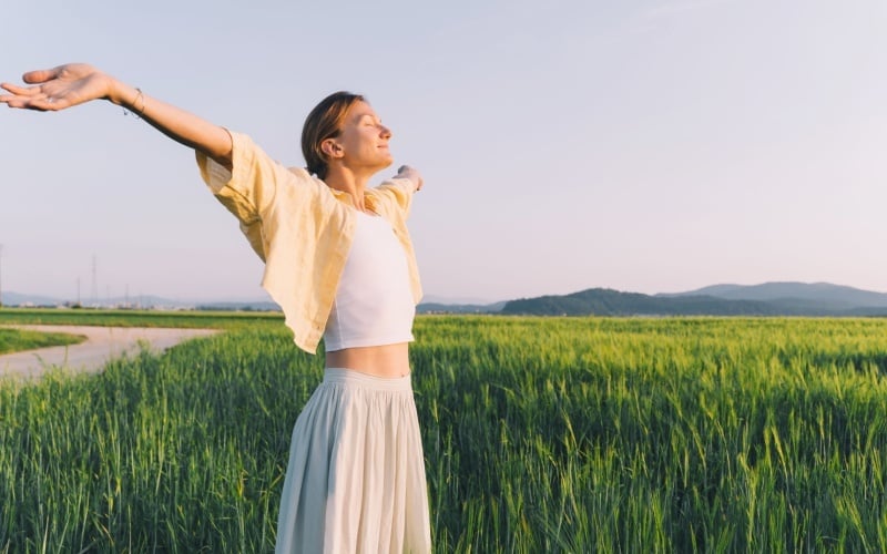 Happy woman is breathing outstretched arms in nature in sunset