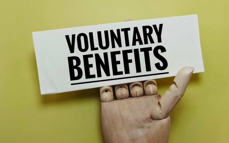 wood hand holding sign that reads voluntary benefits
